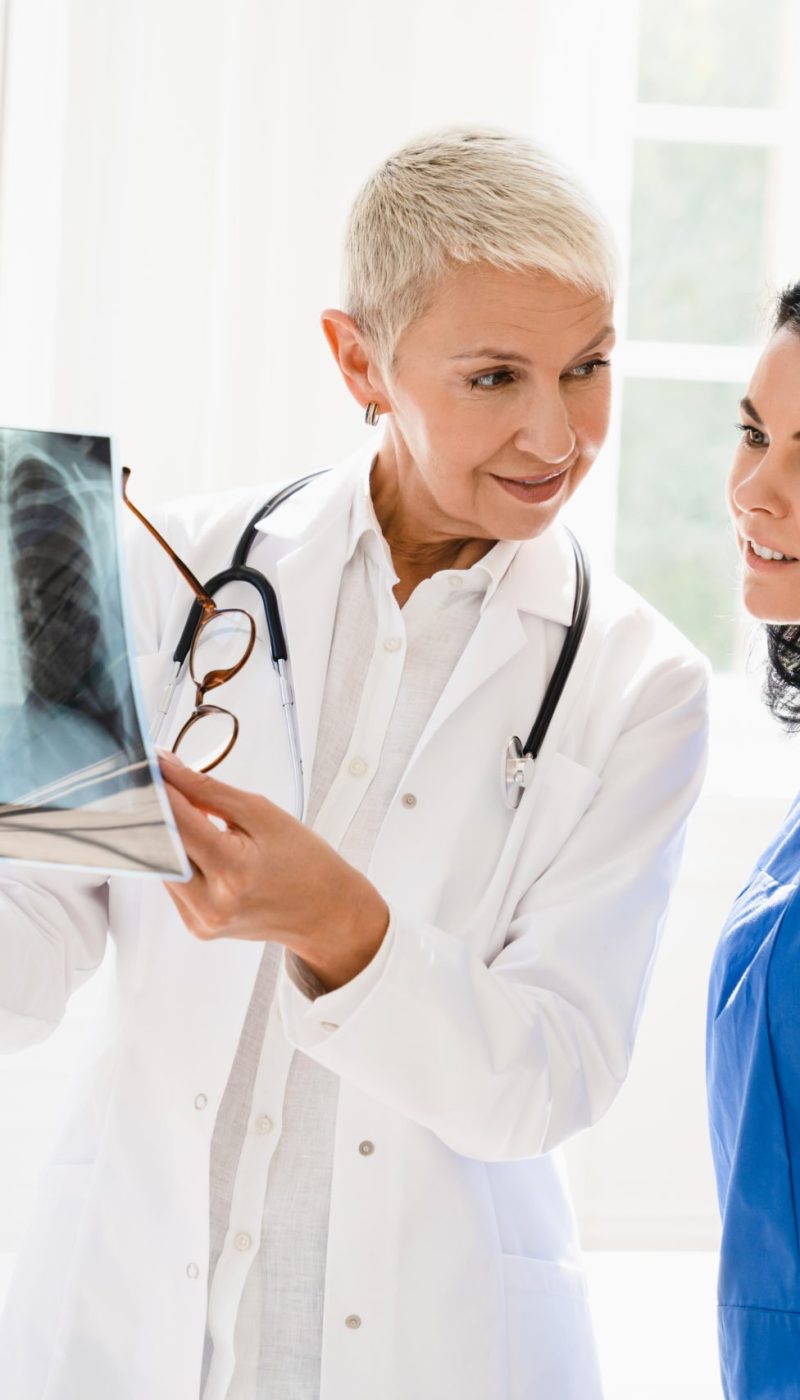 Caucasian senior female doctor showing x-ray image of lungs to medical student intern nurse caregiver, explaining disease illness diagnosis