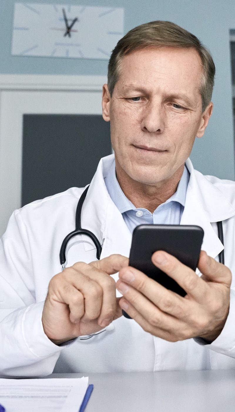 Old male doctor holding cellphone using mobile phone telemedicine technology.